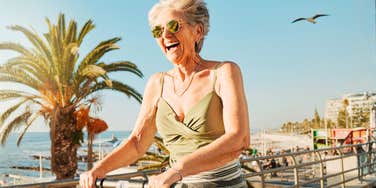 Woman in her sixties smiling while riding a bike outdoors, illustrating brain-boosting habits that support cognitive health later in life
