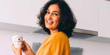 A woman looking back and smiling in a cozy kitchen, capturing the 'radical self-acceptance' and peaceful morning rituals of an empowered woman.