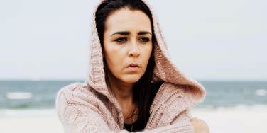 A woman sitting alone on a beach with a sad expression, illustrating the 'secondary loss' and developmental grief felt by parents after the death of a child.