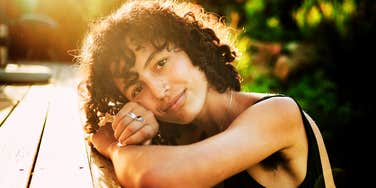 A smiling woman relaxing with her head on her hands.