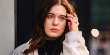 A sad woman sweeping her hair out of her face outdoors, illustrating 'social betrayal trauma' and the difficulty of identifying a covert con-artist.