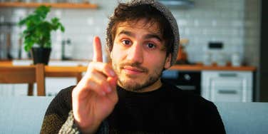 A young man with a beanie on a sofa, captured mid-sentence as he interrupts a conversation, illustrating the common communication mistake men make without realizing it.