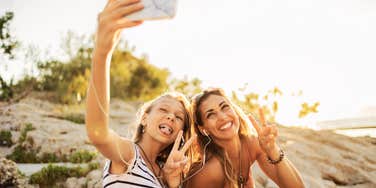 A happy teenage girl and her mother take a sunset selfie on a beach, representing the fleeting moments of connection amidst the hidden challenges of raising teens.