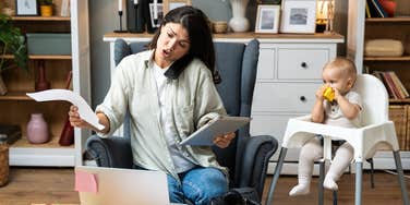 stressed mom working in front of laptop with baby sitting in high chair