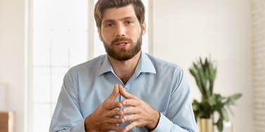 businessman sitting with hands together talking to camera