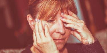 A mature woman with dementia looking down hands on face.