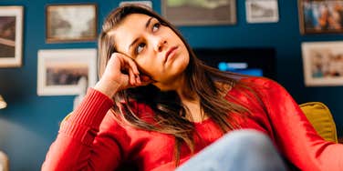 A woman looking anxious and pensive while sitting alone; a visual representation of the 'overthinking' cycle and the internal doubt that reveals a lack of self-trust.