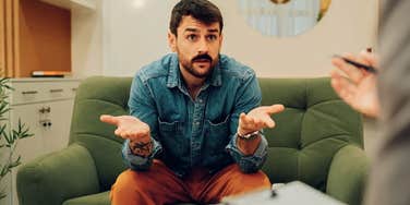 Controlling man looks angry with his hands out on a couch 