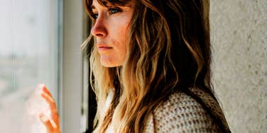 A portrait of a woman in reflection near a window, representing the emotional complexity of navigating her daughters lifelong medical diagnosis.