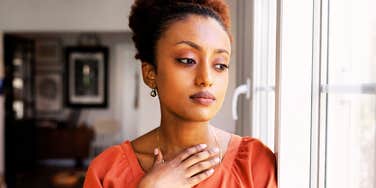 A serious young African woman looking out of a window, capturing the internal 'emotional numbness' of high-functioning depression where one continues to work while feeling nothing.