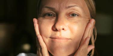 A portrait of a middle-aged woman touching her face with a thoughtful expression.