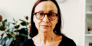 An older woman with red-framed eyeglasses looking seriously at the camera, illustrating 'cognitive appraisal' and the subtle personality changes associated with early-onset dementia.