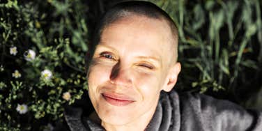 A serene and joyful bald woman smiling laying in grass outdoors; illustrating the hope and radical life changes that can follow a devastating medical diagnosis.