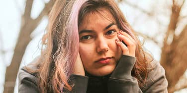 An overwhelmed woman resting her hands on her cheeks with a tired expression, capturing the exact feeling of being burnt out and unable to catch a break.