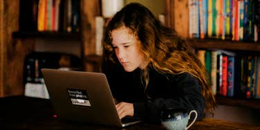 A young girl using a laptop in a bedroom setting; illustrating the moments of digital consumption that can lead to unexpected discoveries about a child's online exposure.