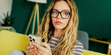 Bright Gen Z woman in glasses holds a smartphone 