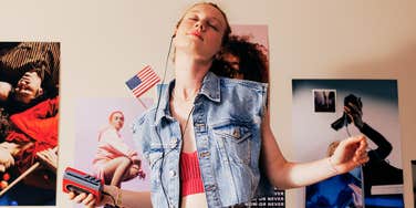 A retro portrait of a young woman wearing headphones connected to a vintage Sony Walkman; illustrating the classic 1980s experience of listening to influential female pop icons in a private bedroom setting.