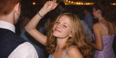 A nostalgic AI image of a high school girl slow-dancing with an ecstatic smile; showing 90s formal wear and dimmed gym lighting, illustrating the romantic energy of the era's classic love songs.