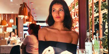 A woman sitting at a cafe table with a calm, discerning expression; illustrating the objective perspective single individuals have when identifying the patterns that newly married couples might overlook.