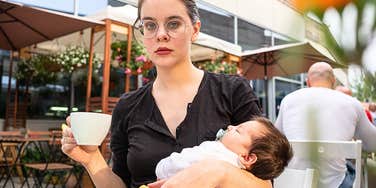 Tired mom who wishes she knew truths before having babies holds her baby in an outdoor cafe