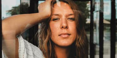 A curious-looking woman leaning on a window with direct eye contact, illustrating 'intellectual inquiry',