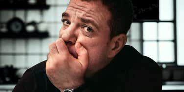 A portrait of a man looking distressed and thoughtful in his kitchen; a visual representation of the internal struggle a father faces when contemplating his children's lives without him.