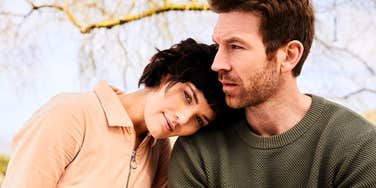 A woman resting her head on her husband's shoulder in a natural outdoor setting; illustrating the 'little things' and subtle gestures of affection that strengthen a marriage even without words.