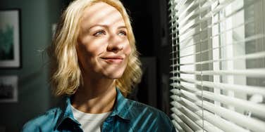 millennial woman looking out window with sun shining