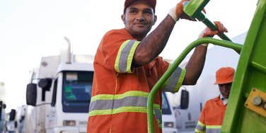 garbage man standing at the back of truck