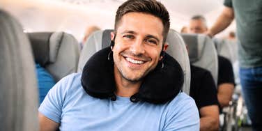 A happy man resting on an airplane with his neck pillow adjusted for maximum support, capturing the 'secret' to avoiding neck pain while sleeping on a plane.