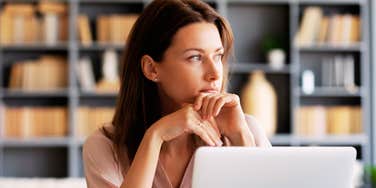 A pensive professional woman at her workspace looking away from her computer toward the window; a visual representation of the psychological shift and 'value misalignment' many Gen X employees are currently facing.