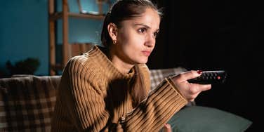 focused woman holding remote and watching tv sitting on couch