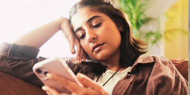 A woman typing on her phone while looking down, disconnected from her surroundings; illustrating the 'digital autopilot' mode that critics say is being exacerbated by tools like ChatGPT.