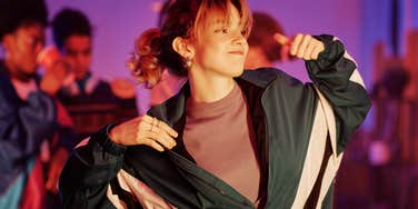A woman with 80s-style hair and jewelry laughing while dancing with a partner in a hazy, neon-lit room, capturing the magic of pre-digital romantic encounters.