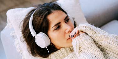 A woman lying down in a quiet room wearing headphones, capturing the relatable moment of using nostalgic media to navigate the emotional pain of a recent breakup.
