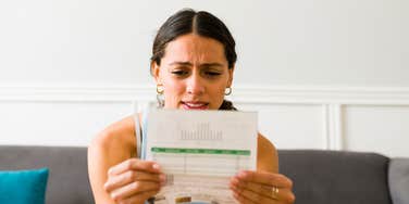 A woman with a pained expression staring at a bill; a visual representation of the 'one responsibility' most people say marks the true transition into adulthood.