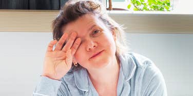 A tired woman in her 50s rubbing her eyes in bed, illustrating the common struggle of poor sleep and the potential for morning refreshment through simple lifestyle fixes.