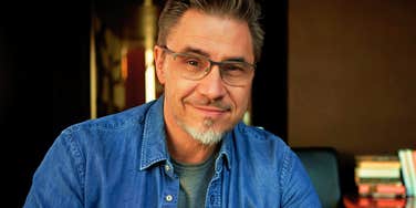 A confident man in his 50s smiling while working on a laptop in a cozy home office, illustrating the active habits that help people over fifty stay visible and relevant.