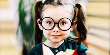 A preschooler with glasses holding a book, capturing 'intellectual curiosity' and the overlooked early-learning milestones that predict academic success.