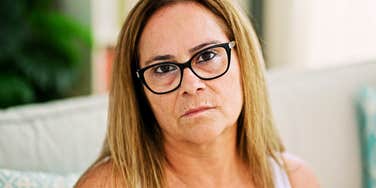 A serious woman sitting alone on a couch, capturing the 'stoic introspection' and the search for closure regarding past life choices.