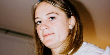 A woman with an aware and pensive expression looking directly at the camera; a visual representation of the hyper-vigilance and 'small' subconscious habits adults carry after a difficult childhood.