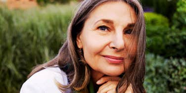A mature woman smiling in a sunlit park.
