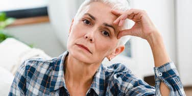 A mature woman with her hand on her head looking pensive, illustrating the 'relational fatigue' and emotional distance often felt in long-term marriages.