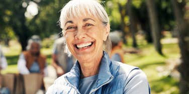 A mature woman volunteer smiling outdoors with food donations; a visual of the small acts of service that rebuild human connection for older adults.