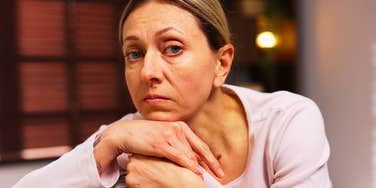 A lonely woman sitting on a couch in the evening light; illustrating the psychological connection between childhood neglect or hurt and the adult tendency to withdraw from others as a safety measure.