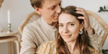 A man tenderly kissing a woman’s head, illustrating the 'safety and security' markers that experts look for in long-term relationship viability.