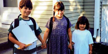A vintage 1997 family photo of three siblings in front of their suburban home, illustrating the 'normal' 90s lifestyle that many now consider a financial luxury.