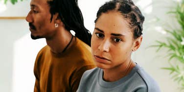 An unhappy couple sits side-by-side on a bed, physically close but emotionally distant, illustrating the "alone together" signs common in struggling relationships.