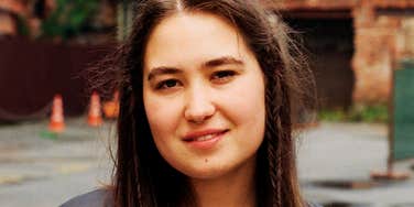 A woman standing in front of an old building, capturing the quiet triumph of someone overcoming social anxiety to finally step back into the world.