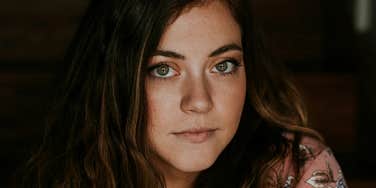 A close-up of a millennial woman with a tired, pensive expression; a visual representation of the psychological burden of never 'switching off'.